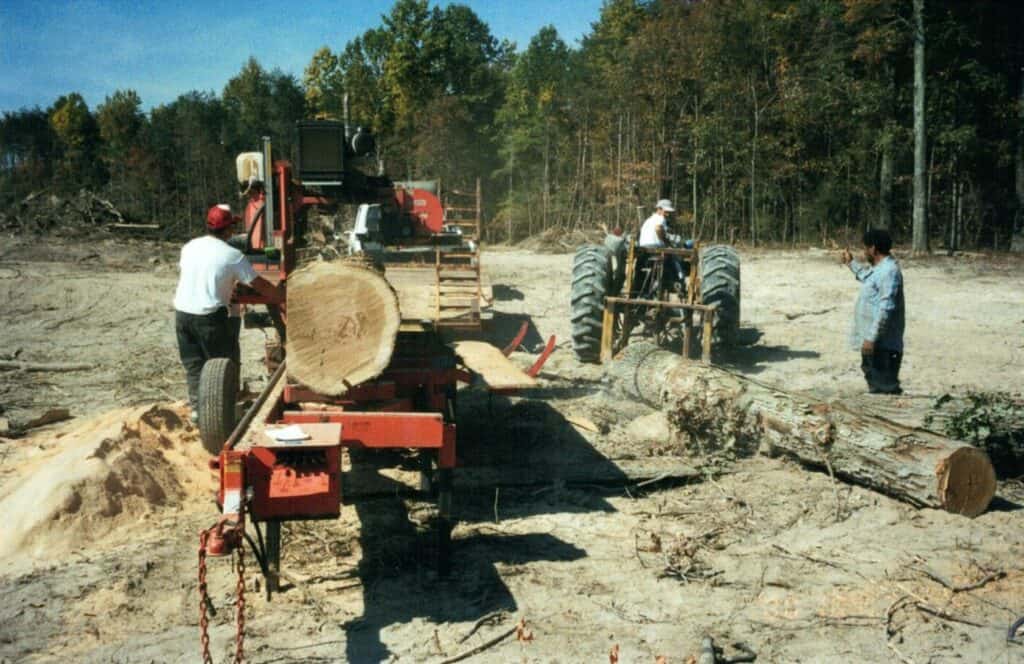 Workers operating sawmill equipment outdoors.