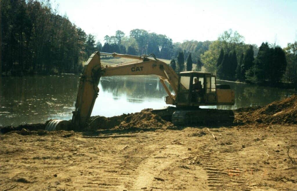 Excavator dredging pond on sunny day