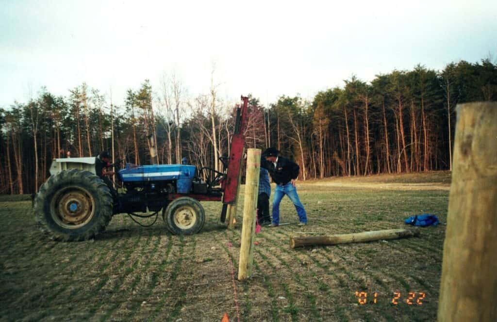 Man working with tractor on fence installation outdoors.