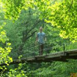 Man standing on forest suspension bridge.