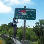 Person posing with Welcome to North Carolina sign.