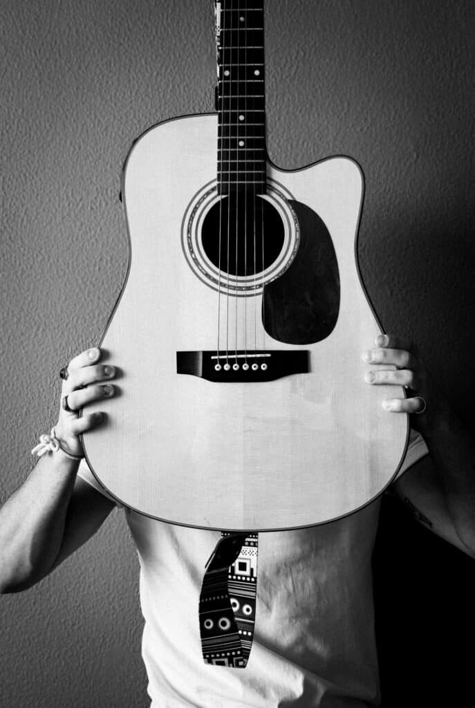 Person holding guitar covering face, black and white photo.