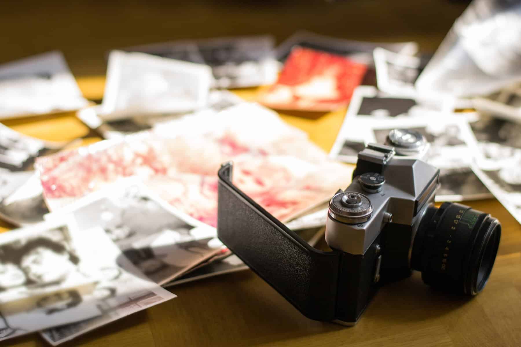 Vintage camera with scattered photographs on table.