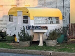 Vintage yellow and white camper trailer with "ENTRANCE" sign.